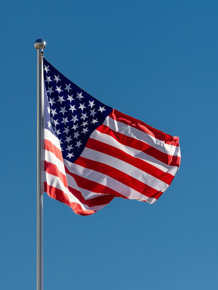 A vibrant American flag waves on a flagpole against a clear blue sky symbolizing patriotism.