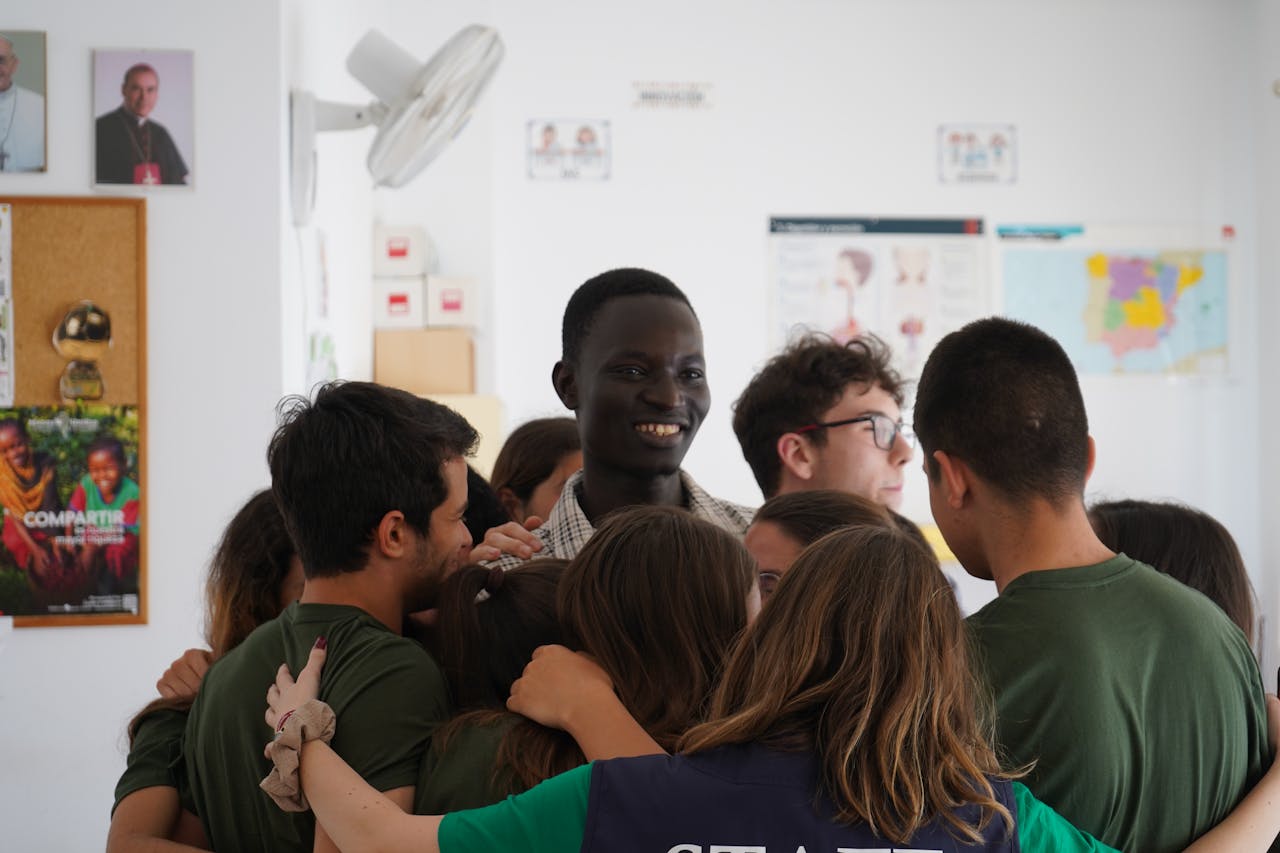A diverse group of young adults share a group hug indoors in a classroom setting, promoting unity and friendship.